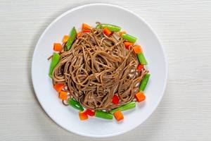 Top view buckwheat noodles with asparagus, carrots and sweet peppers on a white wooden background