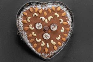 Top view chocolate heart cake with nuts and coconut on black background
