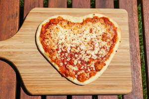 Top View Food Photo of Fresh Heart Shaped Pizza with Tomato Sauce and Cheese on a Wooden Cutting Board