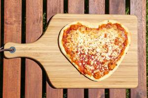 Top View Food Photo of Heart Shaped Margarita Pizza on Wooden Cutting Board
