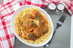 Top View Food Photo of Pasta with Meat Balls and Cheese seasoned with Salt and Pepper next to a Fork and Kitchen Cloth on Wooden Table