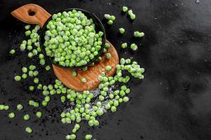Top view green young peas in a bowl and scattered on a black background (Flip 2019)