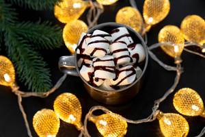 Top view mug with hot chocolate and marshmallows on a black background with a luminous garland (Flip 2019)