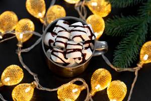 Top view mug with hot chocolate and marshmallows on a black background with a luminous garland
