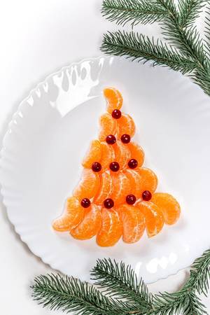 Top view of a Christmas tree made from mandarin and cranberries on a white plate