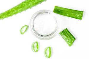 Top view of aloe Vera gel in a glass jar with fresh aloe leaves on a white background (Flip 2020)