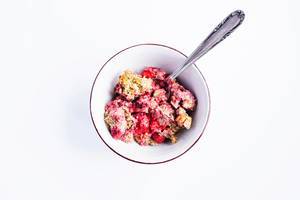 Top view of baked strawberry walnuts oatmeal in a bowl with spoon on white background