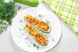 Top view of baked zucchini halves with vegetables, couscous and greens on a white wooden background with fresh zucchini and dill (Flip 2019)