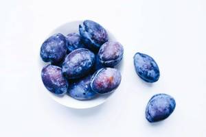 Top view of blue plums in a bowl on white background