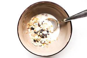 Top view of bowl of raisins muesli and milk on white background