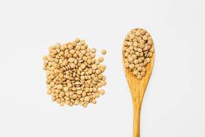 Top view of brown lentils on a wooden spoon isolated on white background