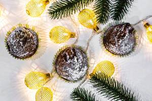 Top view of chocolate cupcakes with christmas tree branches and a luminous garland