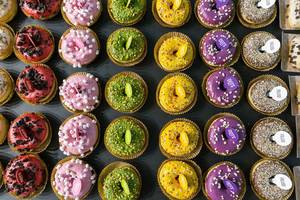 Top view of colorful doughnuts by Dots original Rainbow, with  Pistachio, Purple White, Marshmallow with pink icing and and biscuit crumbles