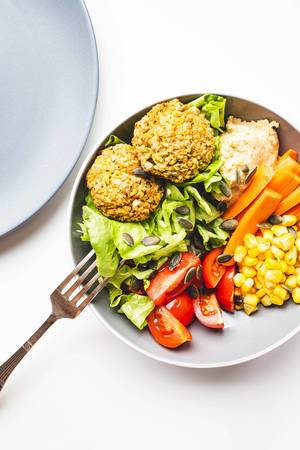 Top view of falafel buddha bowl with vegetables and hummus with fork and plate