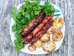 Top view of fried zucchini, grilled sausages and greens on old wooden background
