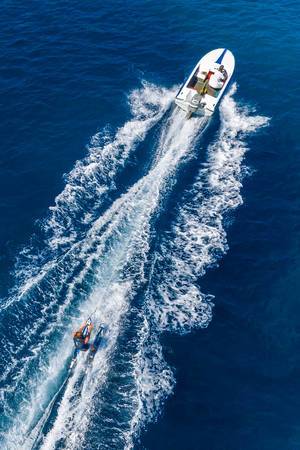 Top view of man on waterskis during vacation, motor sports boat and breaking waves on the blue sea of Argolic Gulf