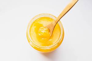 Top view of organic honey in a glass jar with wooden spoon on white background