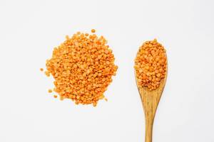 Top view of red lentils on a wooden spoon on white background