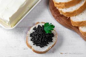 Top view of sandwich with black caviar on white wooden background