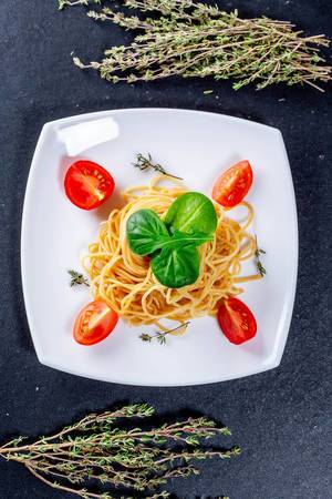 Top view of spaghetti with tomatoes and greens on black background