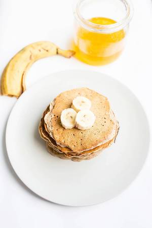 Top view of stacked vegan pancakes with honey and banana