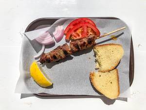 Top view of the national greek dish Souvlaki: Meat skewer with tomatoes, onions, lemon and bread, on a white table