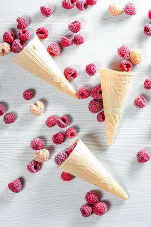 Top view of waffle cone with frozen raspberry berries on white wooden background (Flip 2019)