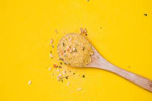 Top view of wooden spoon with yellow spice on yellow background