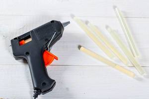 Top View Photo of Black Hot Glue Gun with Glue Sticks on White Wooden Table