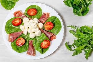 Top view salad with jamon, mozzarella, tomatoes and herbs on a white plate (Flip 2019)