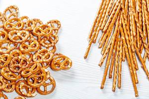 Top view salted straws and pretzels on white wooden background