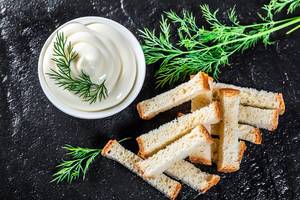 Top view white sauce and crackers with fresh dill on black stone background