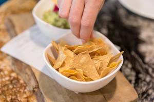 Tortilla chips to dip in guacamole (avocado cream) served on a wooden beam at Fit Kitchen Restaurant in Barcelona, Spain