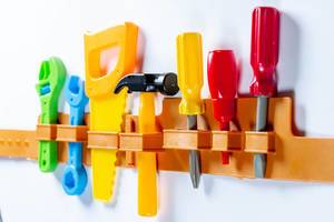 Toy Tools like Saw, Hammer and Screwdrivers hanging on a white Wall