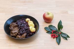 Traditional beef stew with apple beetroot salad and potato dumplings with a twig and an apple on a wooden table