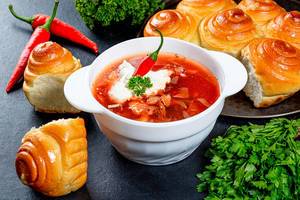 Traditional Ukrainian borscht with meat, vegetables and sour cream on a black background
