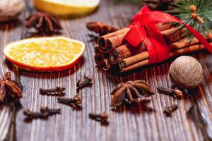 Traditional winter spices: anise, cinnamon, cloves and nutmeg with dried lemon and orange slices on a brown wood background