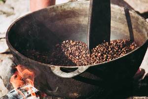 traditionelles Rösten von Kaffeebohnen in Metallpfanne über offenem Feuer