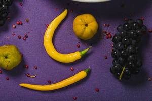 Trauben, gelbe Chilischoten und Quitte auf einem lila Tisch