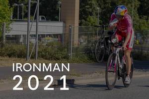 Triathlon participant ans sportsman drinks during bike race, next to the picture title "Ironman 2021"