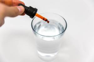 Tropfpipette träufelt Cannabidiol ( CBD) Öl von Braineffect Recover in ein Wasserglas auf weißem Untergrund