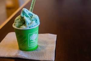 Türkisblaue Eiscreme mit Kaugummi-Geschmack mit Kunststofflöffel in grünem Becher