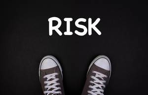 Turnschuhe stehen auf schwarzem Hintergrund, vor der Aufschrift "risk" - Risiko