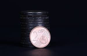 Two Euro cent coin placed in front of piles of coins
