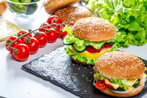 Two homemade hamburgers with fresh vegetables on black stone tray