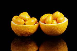 Two orange halves full with kumquats fruits, black background (Flip 2019)