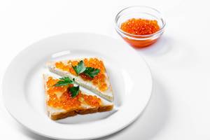 Two triangular sandwiches with salted red caviar on white background