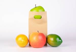 Umweltfreundliche Papiertüte mit Früchten wie Mango, Orange und Äpfeln vor weißem Hintergrund