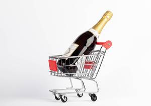 Ungeöffnete Champagnerflasche steht in kleinem Einkaufswagen vor weißem Hintergrund