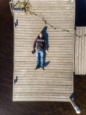Urlauber macht ein Drohnen-Selfie, während er im Asics-Pulli auf einem Holzsteg unter der Sonne am nordischen Päijänne-See liegt